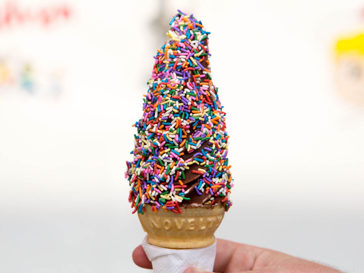 A very tall scoop of ice cream on a cake cone covered in rainbow sprinkles.