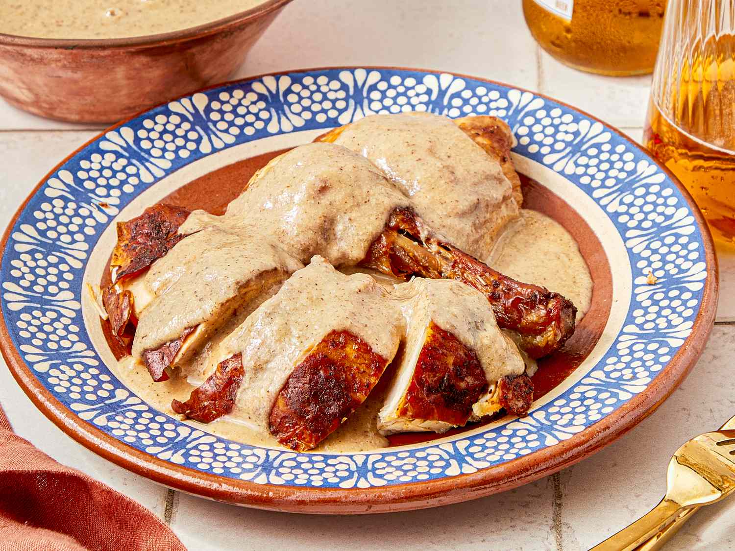 A plate of mole blanco sauce over chicken served on a decorative dish with accompanying dinnerware visible