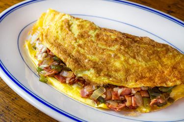 A Western omelette with bell peppers, onion, ham, and cheese on an oval plate.