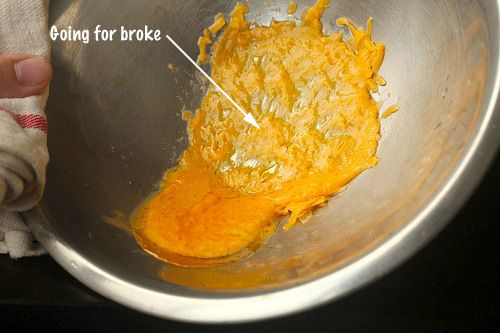 Broken melted cheese in a metal bowl.