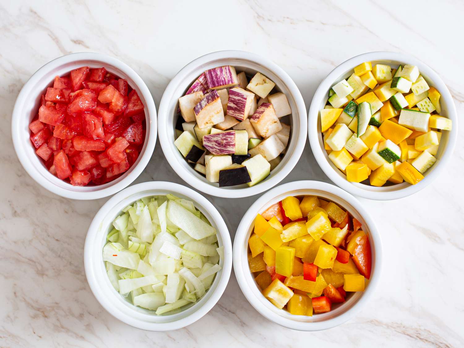 Chopped vegetables sorted into small bowls placed on a marble surface