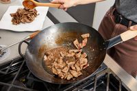 Person cooking in a Mammafong Pre-Seasoned Blue Carbon Steel Flat-Bottom Pow Wok