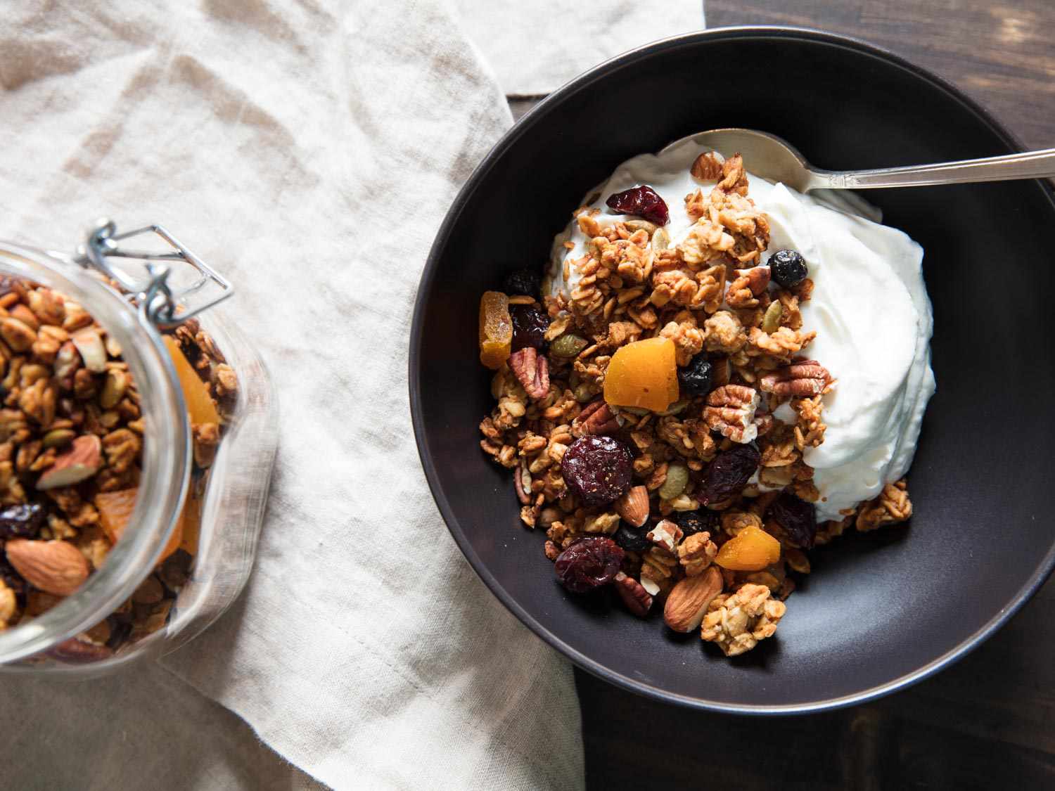 A bowl of homemade granola with yogurt, next to an open jar of granola. 