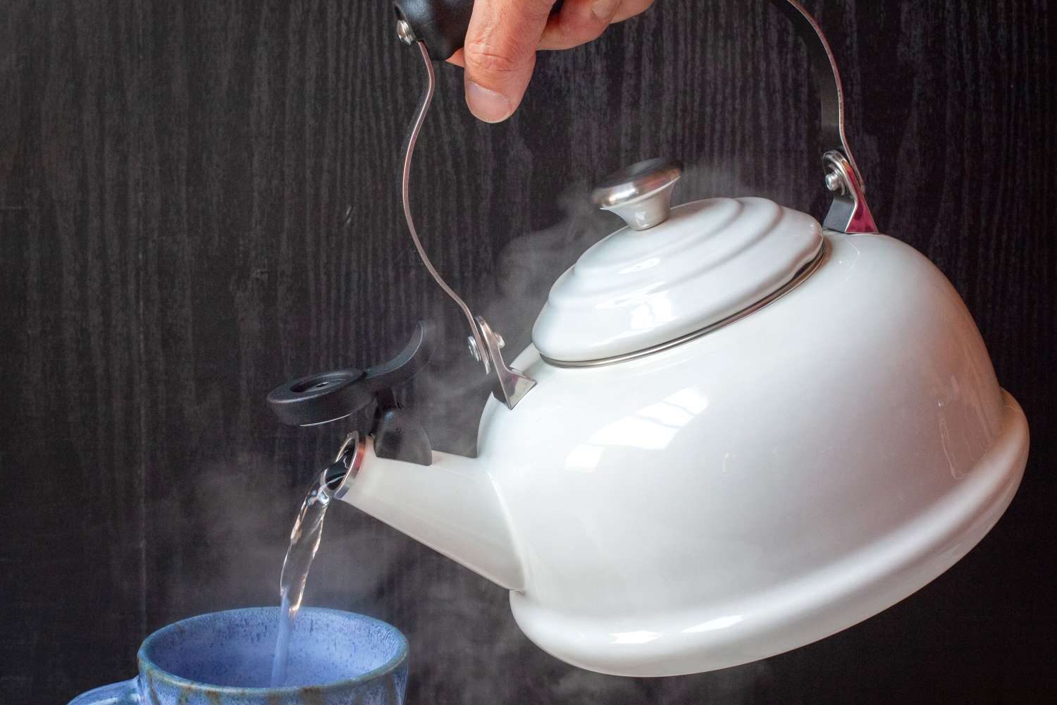 A hand pouring hot water from a kettle into a cup