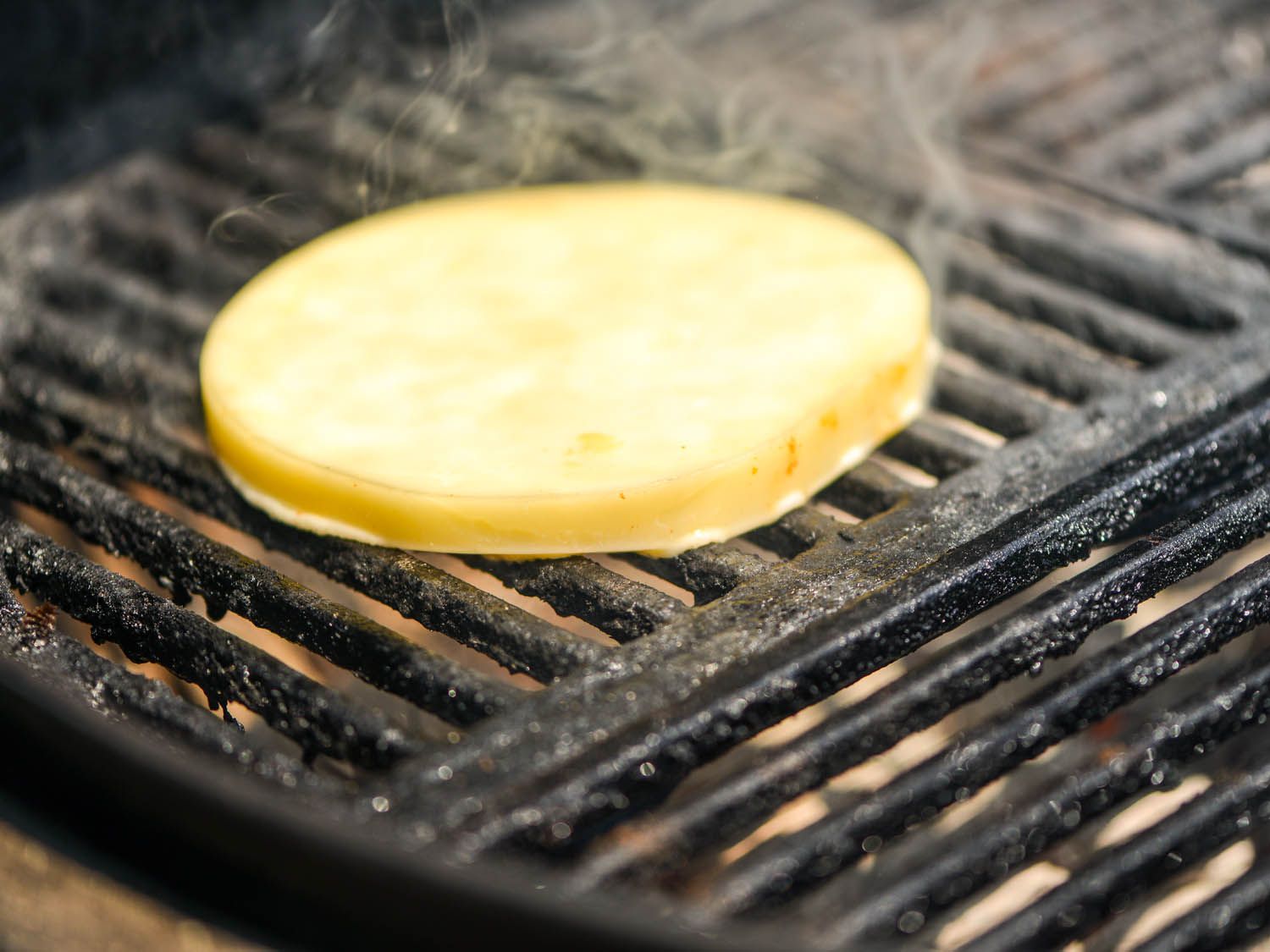 A thick slice of provolone sizzles on the grill grate.