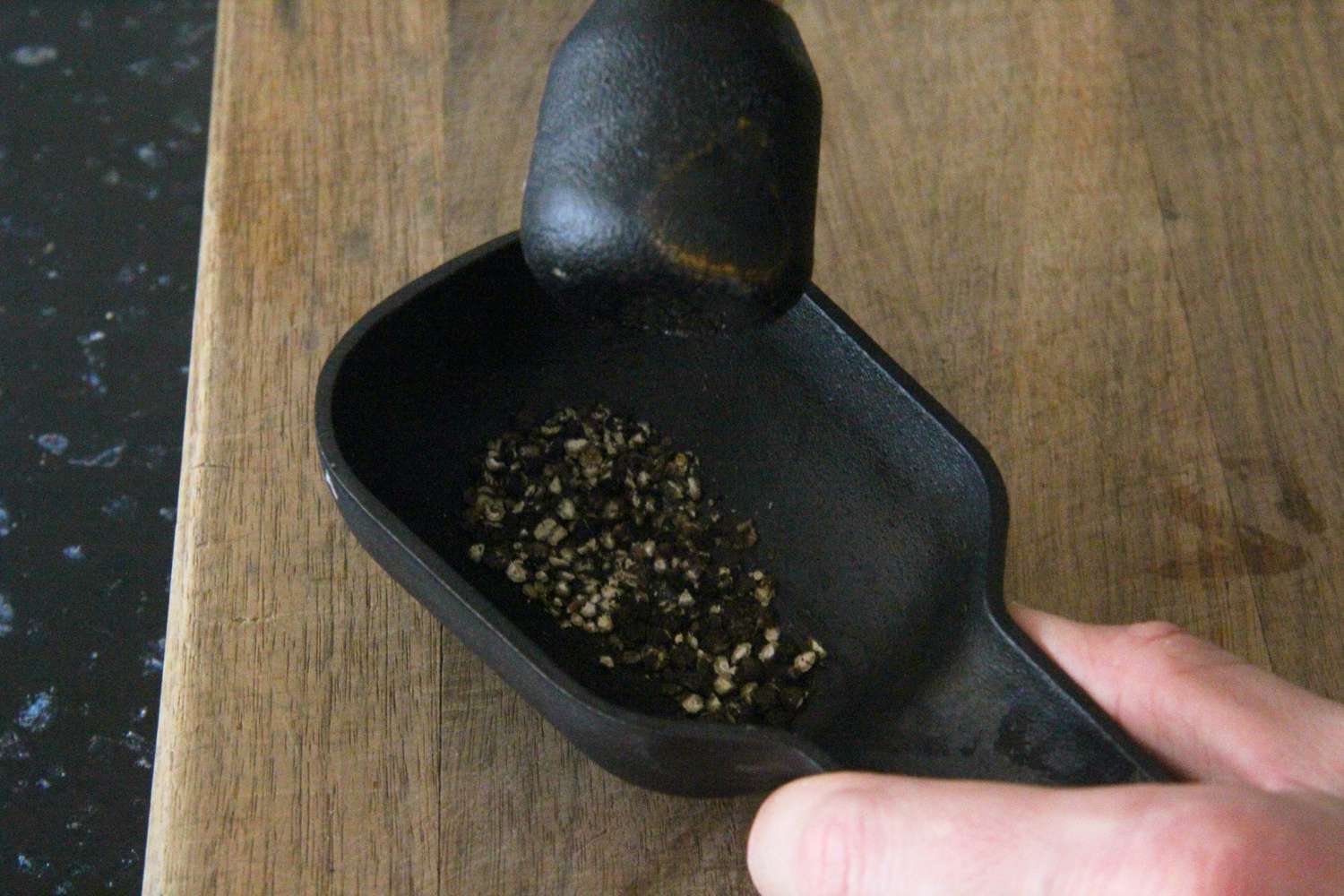 crushing black pepper with a black cast iron mortar and pestle