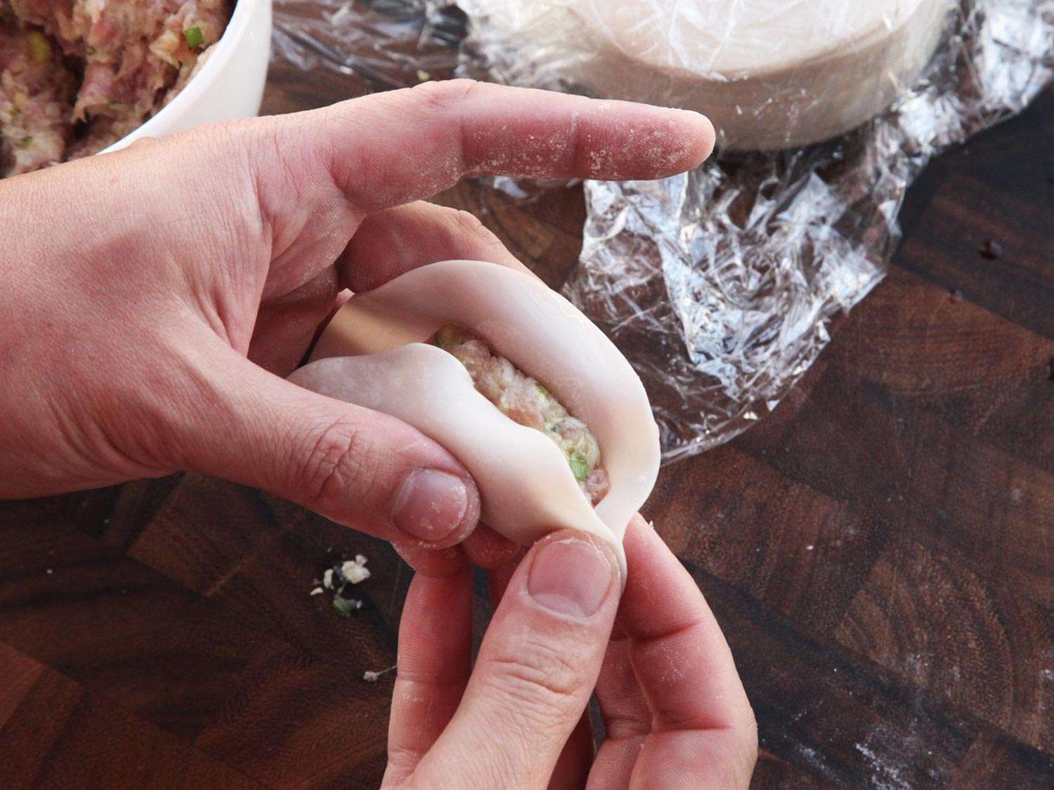 Sealing a round dumpling wrapper filled with ground pork and minced cabbage.
