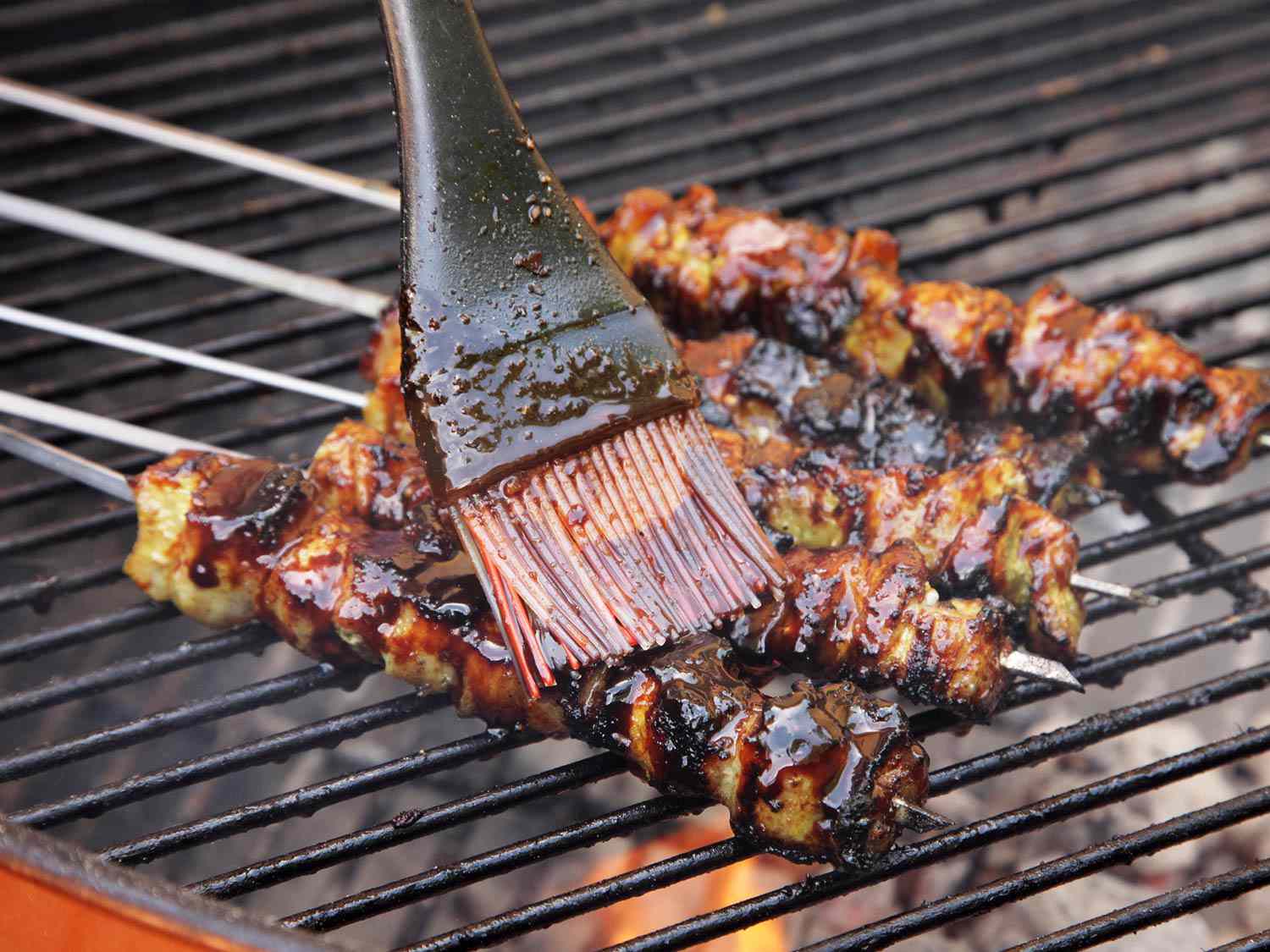 Brushing glaze on pork satays that are cooking on a grill.
