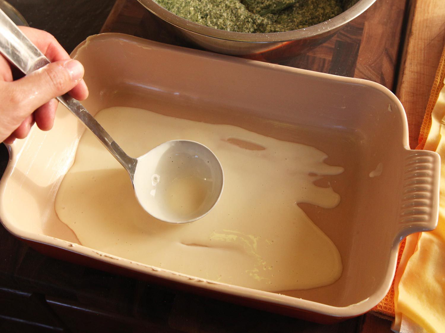 Ladling a thin layer of white sauce on the bottom of the baking dish