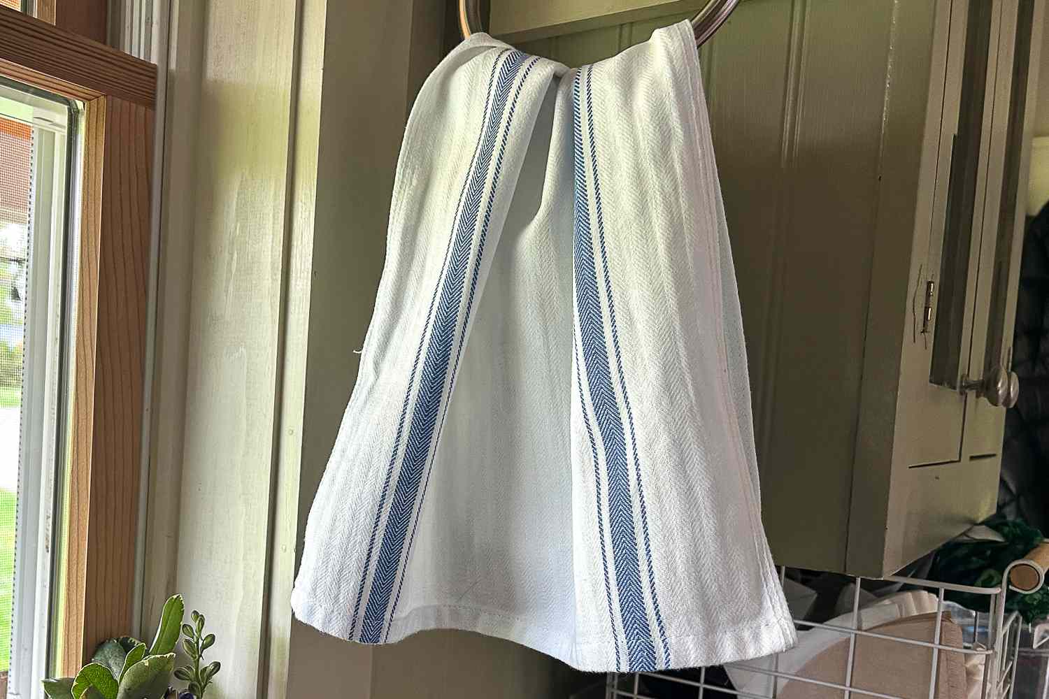 A white towel with blue stripes hanging on a metal ring near a wooden-framed window in a kitchen area