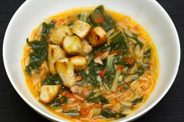 Overhead view of Swiss chard and pasta soup in a deep white bowl.