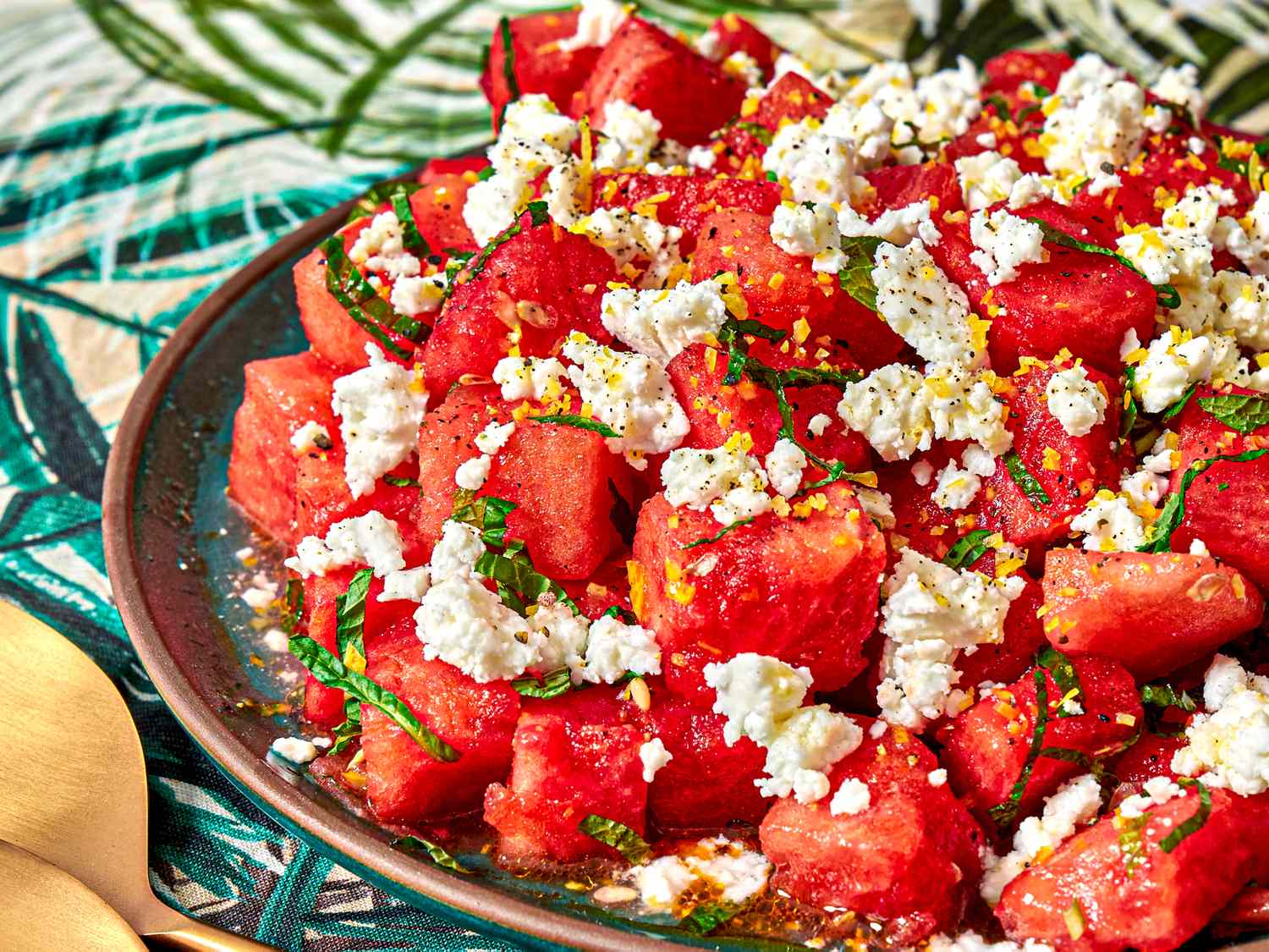 Plate of diced watermelon topped with crumbled cheese and herbs