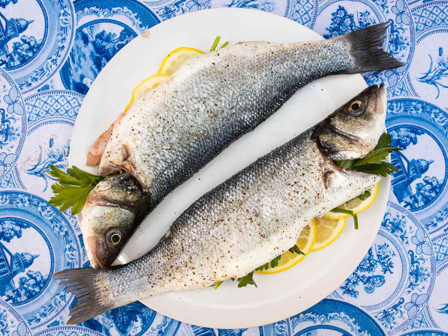 Overhead view of two whole fish on a plate, stuffed with lemon slices and parsley, ready to be grilled.
