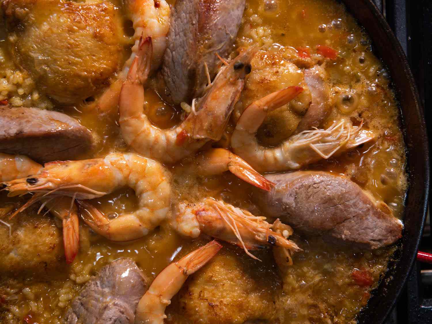 Overhead of stovetop paella simmering in a large pan
