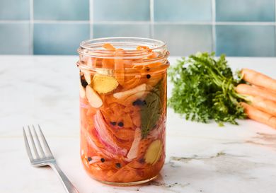 carrot ribbons in a jar with a fork on the side, with blue tile backsplash