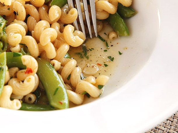 A fork draws the pasta and vegetables back to reveal an emulsified sauce pooling slightly in the bottom of a white bowl.