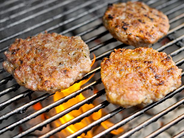 Three breakfast sausage patties cooking on a grill. 