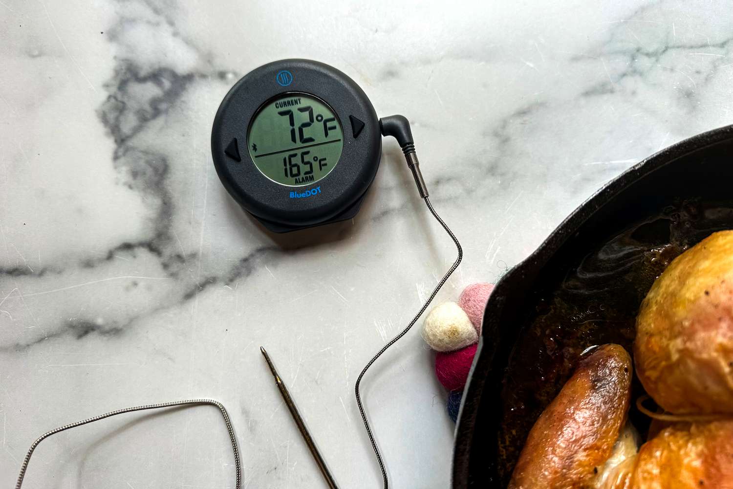 A small digital thermometer with a probe next to a cast iron pan.