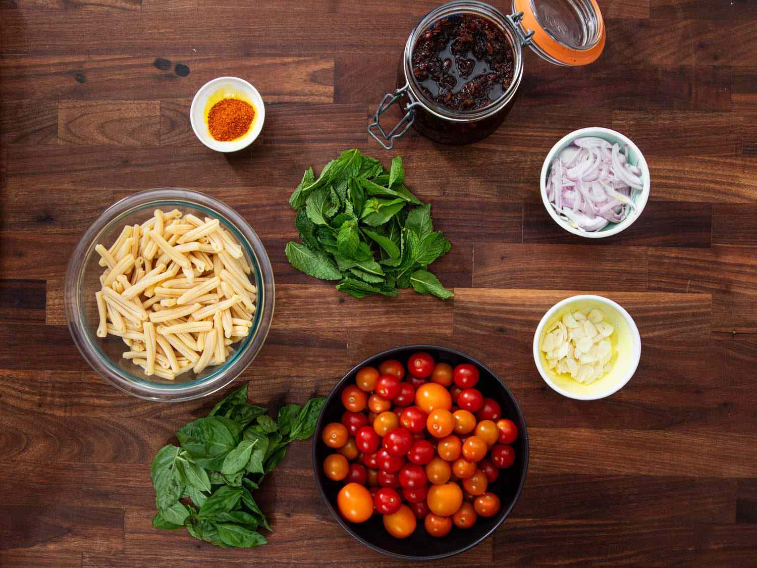 Ingredients for the pasta dish: casarecce pasta, sliced shallots, sliced garlic, red and orange cherry tomatoes, XO sauce, ground dried Thai chiles, fresh mint and basil leaves.