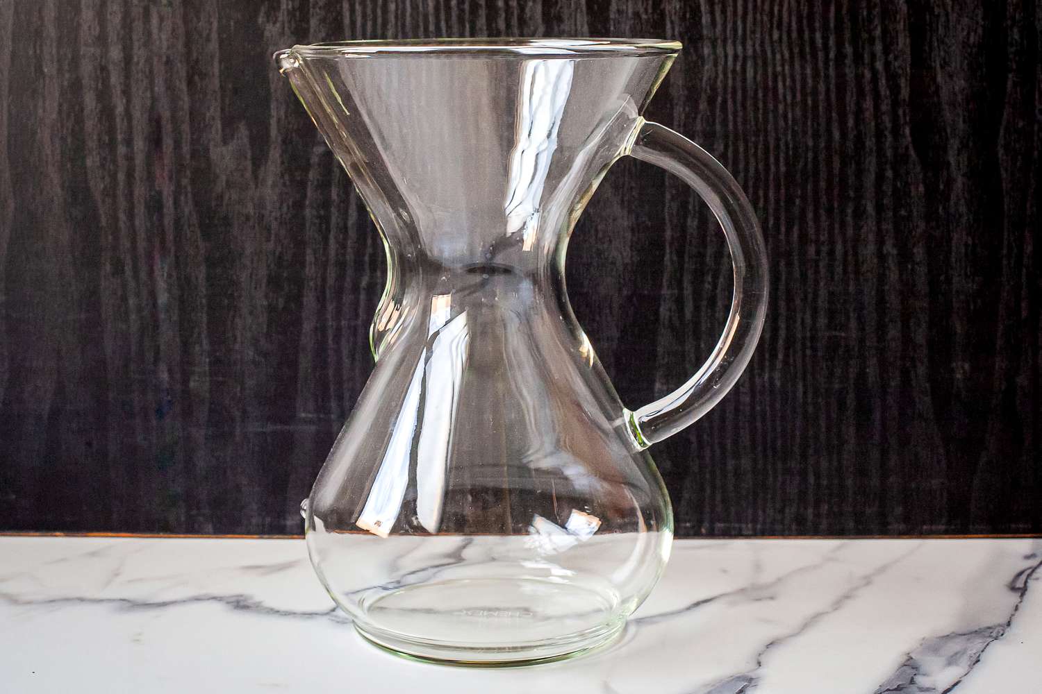 A clear glass Chemex coffee maker placed on a marble surface
