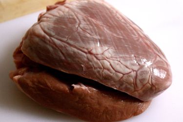 An uncooked beef heart on a white cutting board.