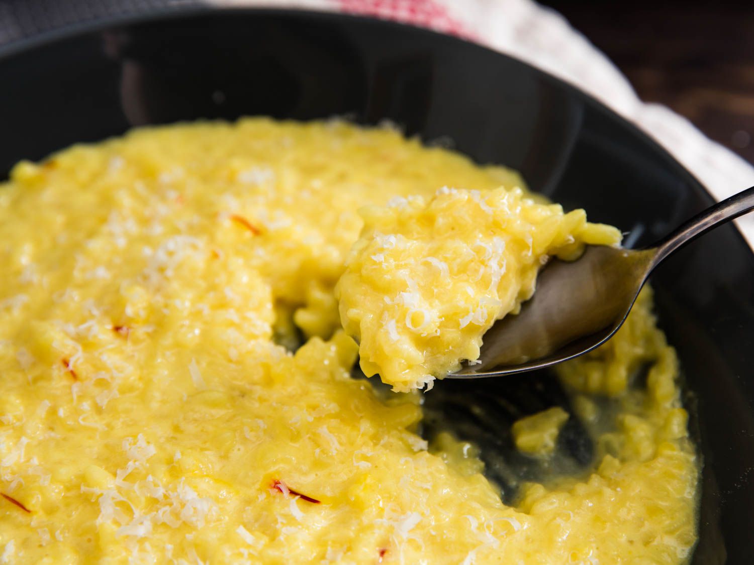 A spoon of risotto alla milanese lifting from the bowl it's taken from. 