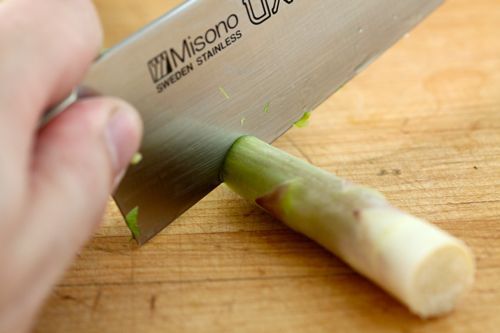Asparagus being cut just above the white part of the stalk.