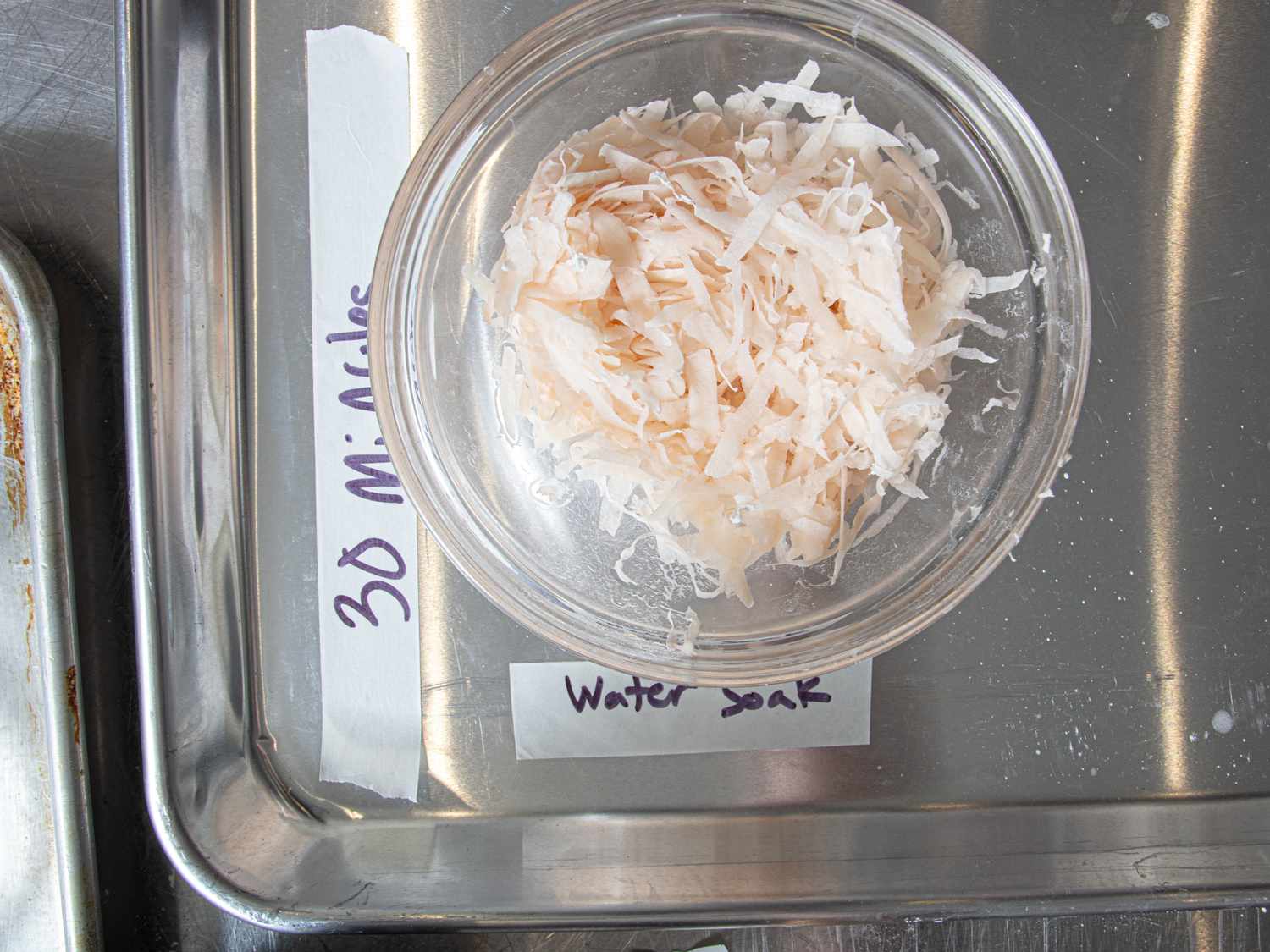 Shredded white material in a glass bowl placed on a metal tray labeled for a 30minute water soak