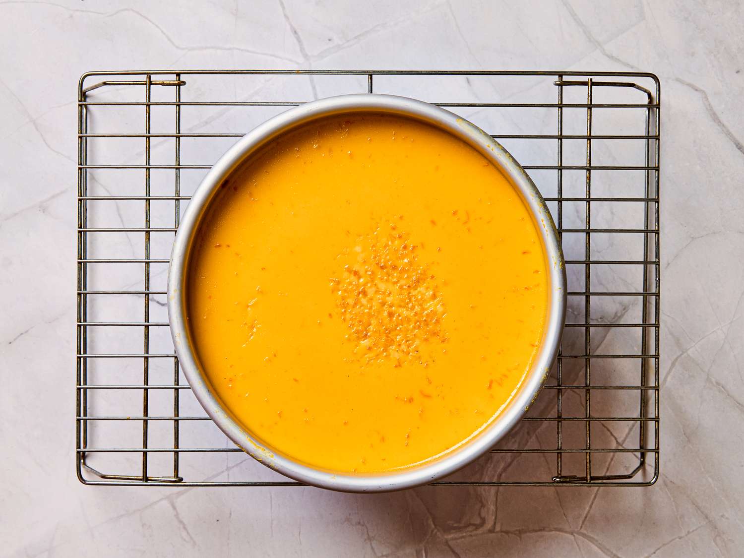 A round orangecolored flan in a baking dish on a cooling rack