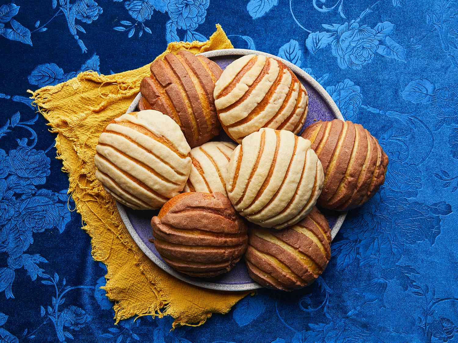 Finished conchas on a plate on a yellow napkin one a blue, floral tablecloth