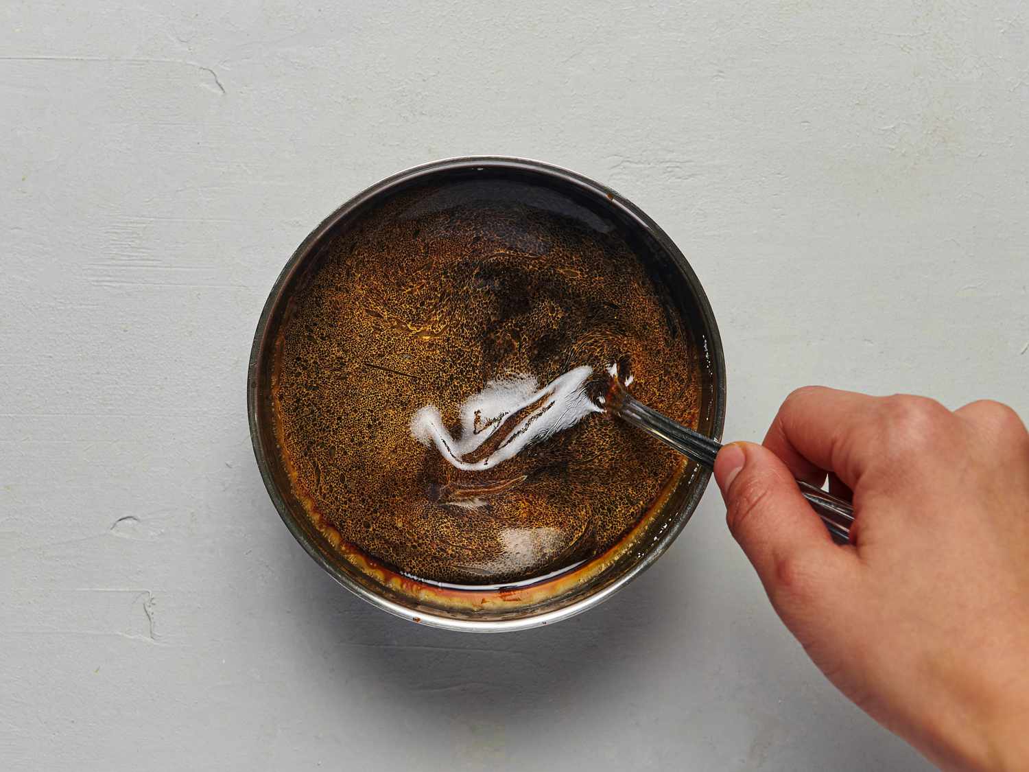 Sugar, chicken stock, soy sauce, wine, vinegar, cornstarch, and sesame oil combined in a small bowl. The sauce is being stirred by a hand holding a metal spoon.