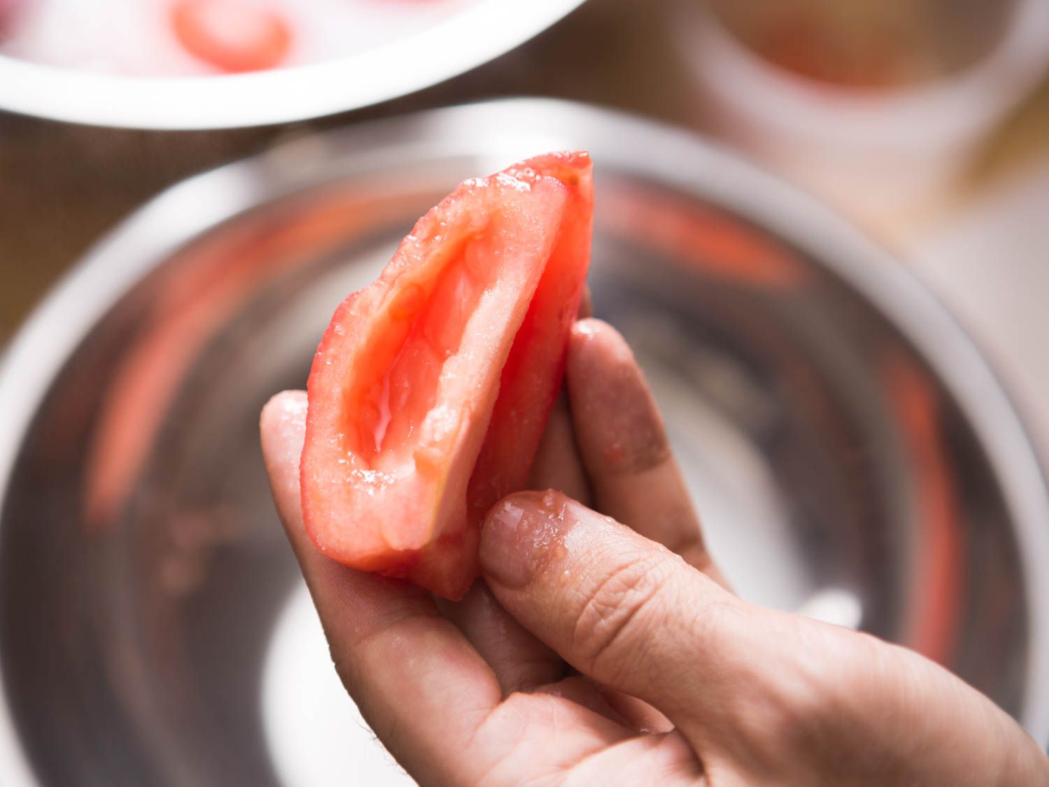 A peeled and seeded tomato quarter is held up to the camera.