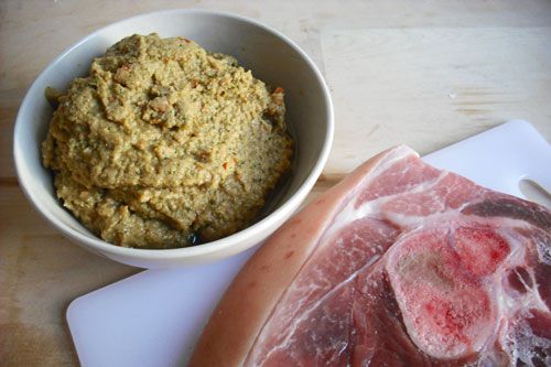 A bowl of curry paste next to a piece of raw pork shoulder.
