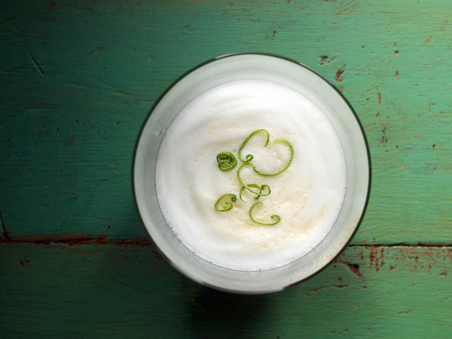 Overhead view of a lemongrass sour, garnished with shreds of lemon zest.