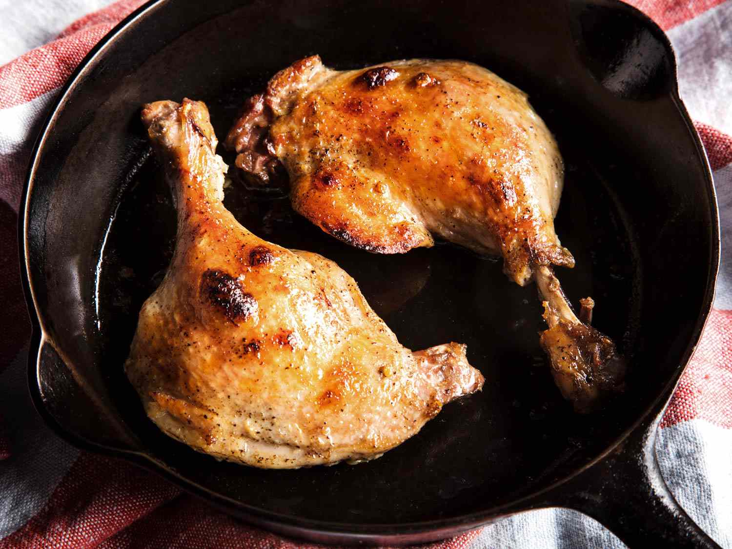 Confit duck legs with browned and crisp skin, in a cast iron skillet.