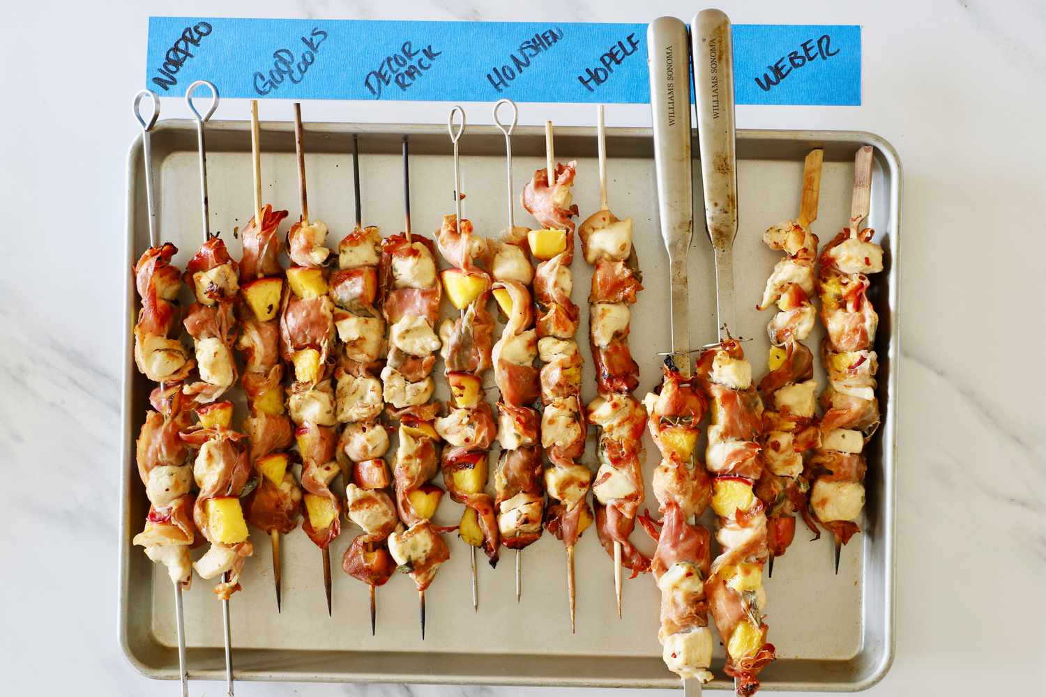 Multiple skewers (wooden and stainless steel) on a sheet tray