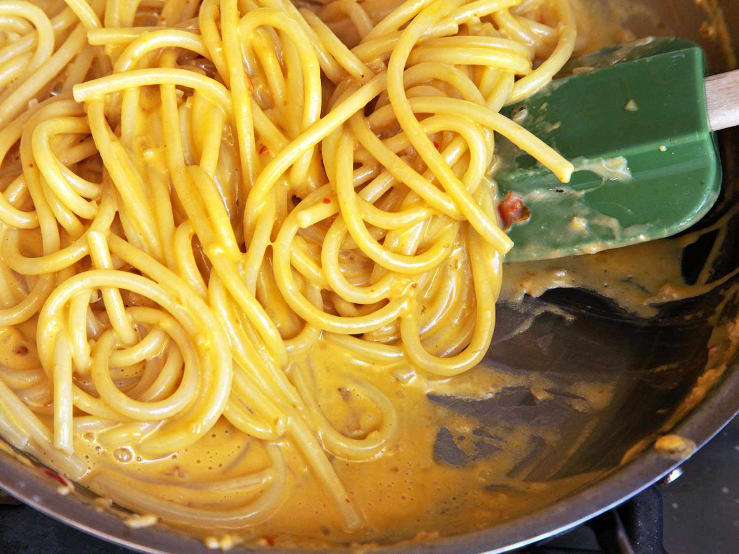 Close-up of sauced sea urchin pasta in the skillet, being stirred by a rubber spatula.