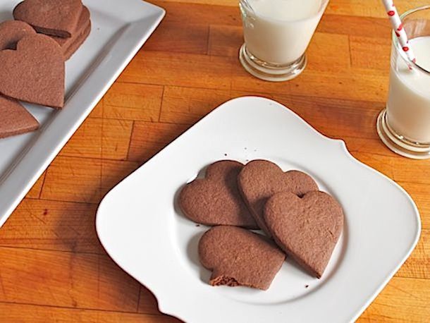 A white plate and platter piled high with gluten-free spicy hot chocolate cookies. Glasses of milk are close at hand.
