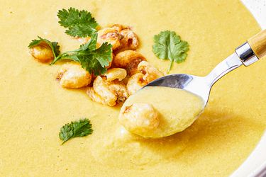 A spoonful of creamy corn soup with garnishes including herbs and toasted corn