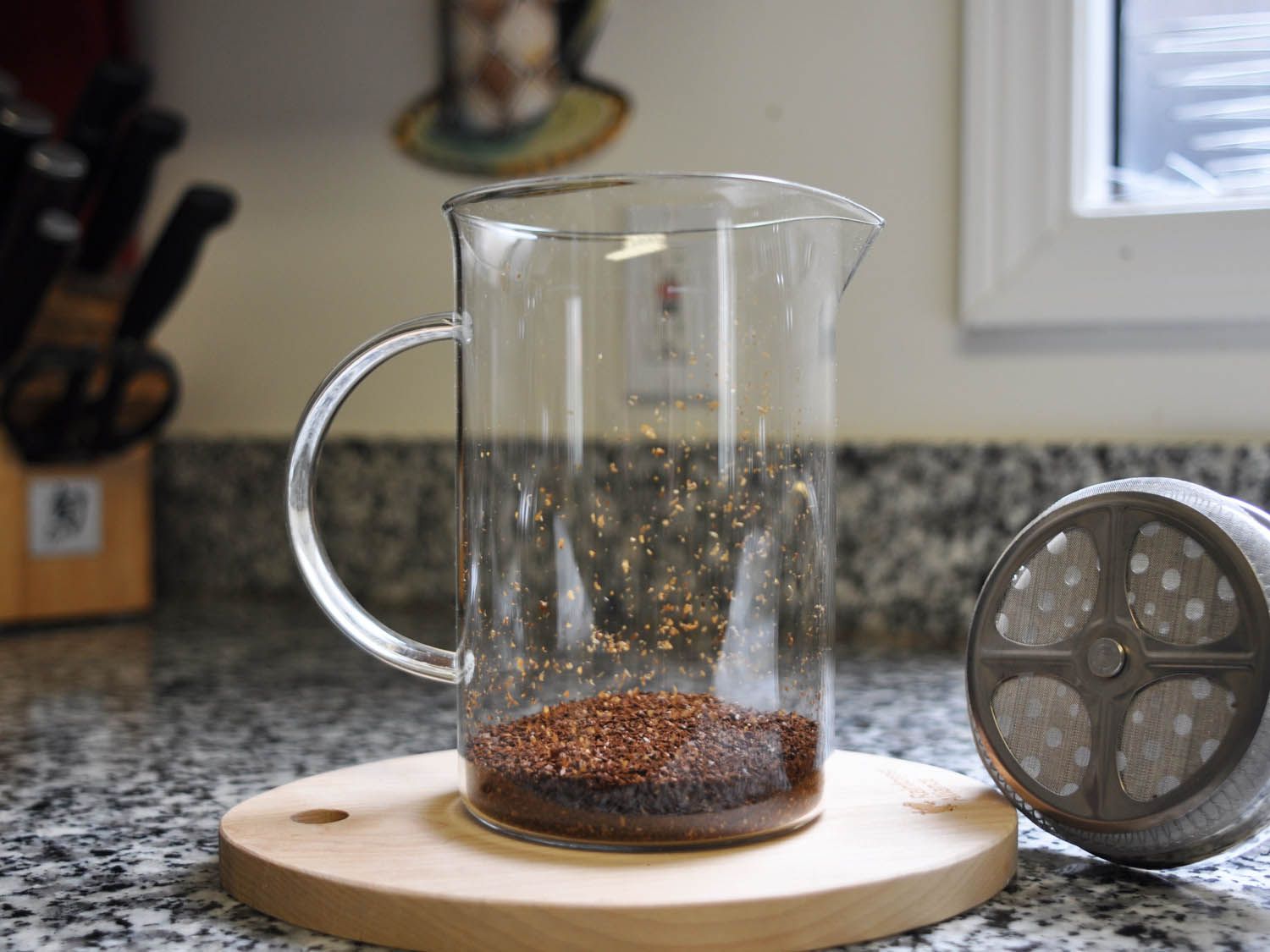 A glass French press with dry coffee grounds poured into it.