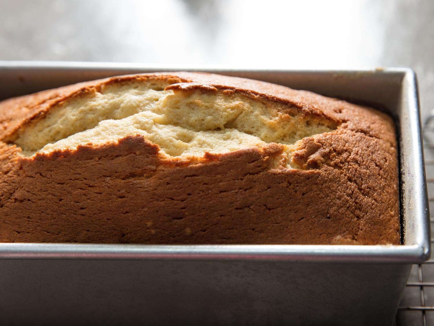 A just baked pound cake in a loaf pan, with a golden-brown crust and a deep crack down the center.