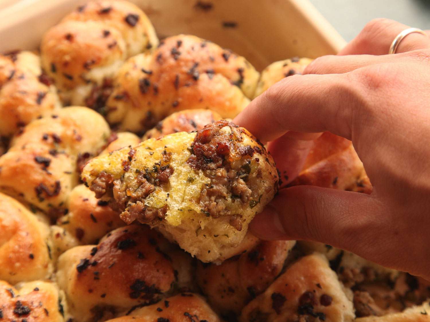 Close-up of a hand picking up a pull-apart stuffing roll flavored with sausage, aromatics, and sausage