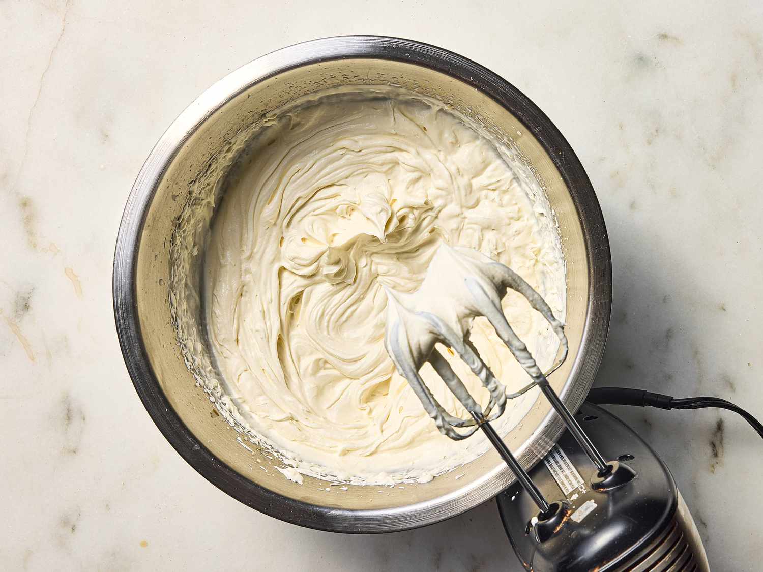 beating frosting until theres peaks with a hand mixer in a metal bowl 
