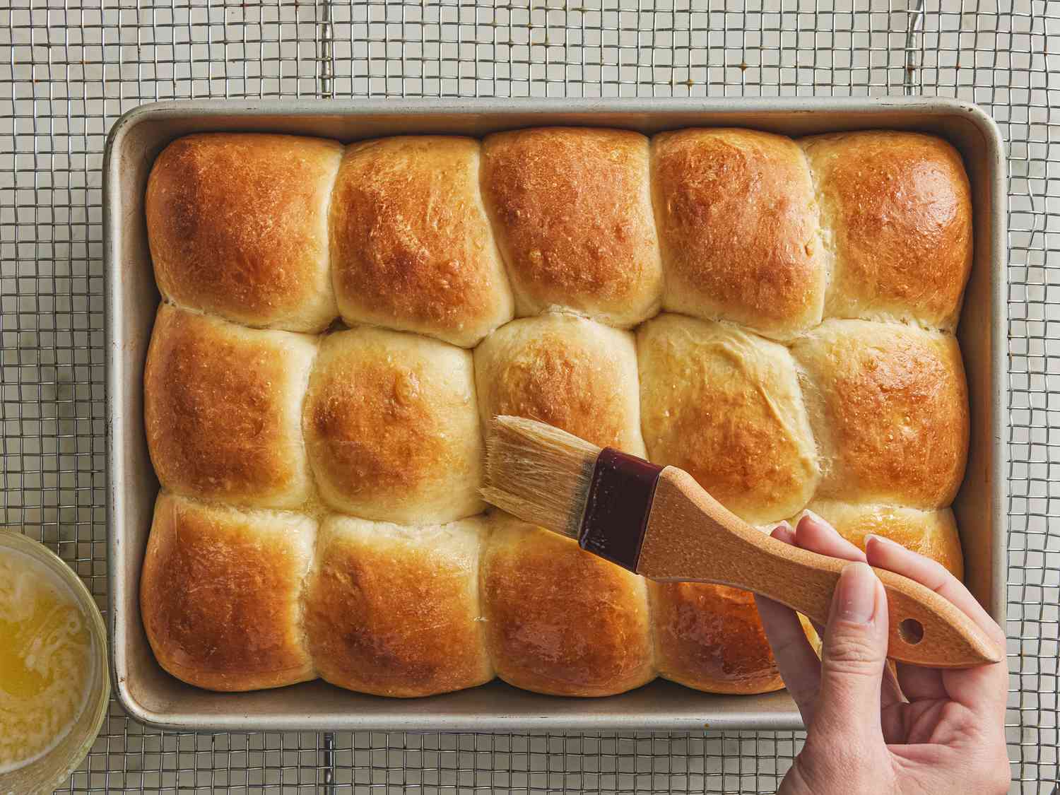 Cooling parkerhouse rolls in a baking pan, being brushed with melted butter 