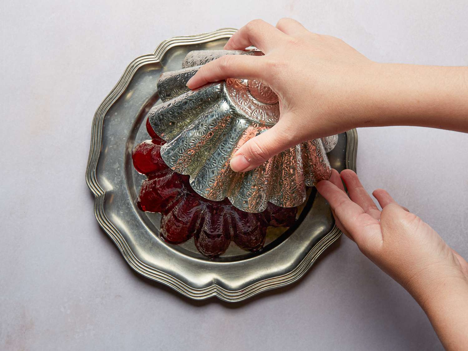 hand inverting mold onto plate, with cranberry sauce releasing onto silver plate. 