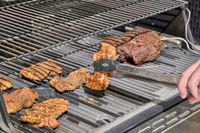 A person cooks chicken in the Masterbuilt Gravity Series 1150 Digital Charcoal Grill and Smoker