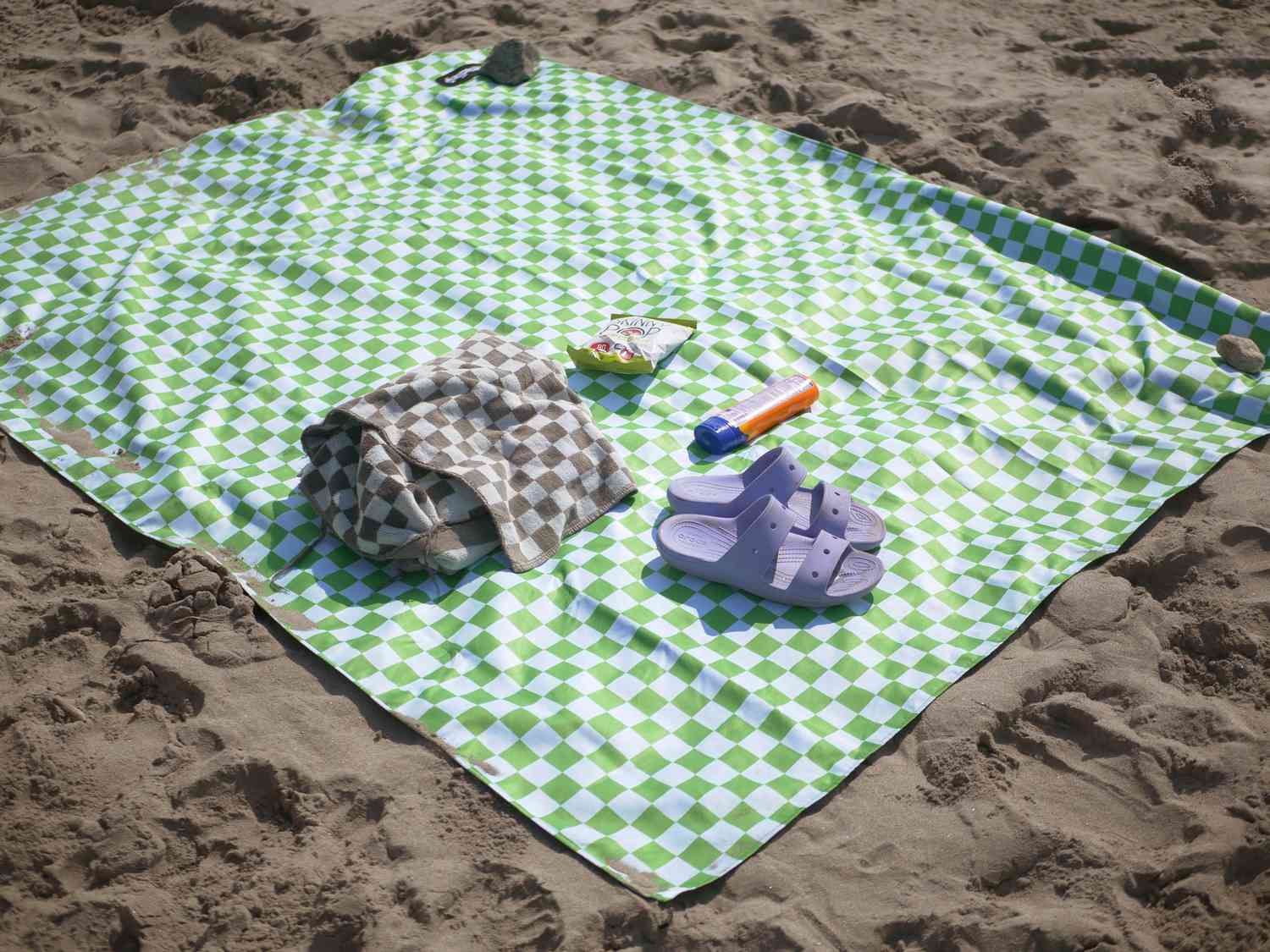 nomadix picnic blanket on the beach with a towel, popcorn, sunscreen, and sandals