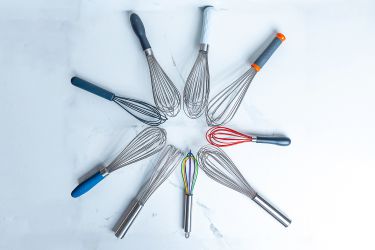 Nine whisks arranged in a circle on a white marble countertop