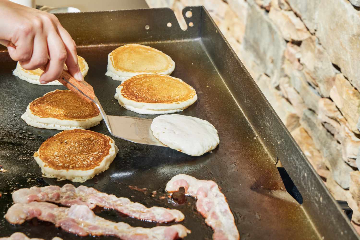 A person cooks pancakes on the Blackstone 1554 Cooking 4 Burner Flat Top Gas Grill