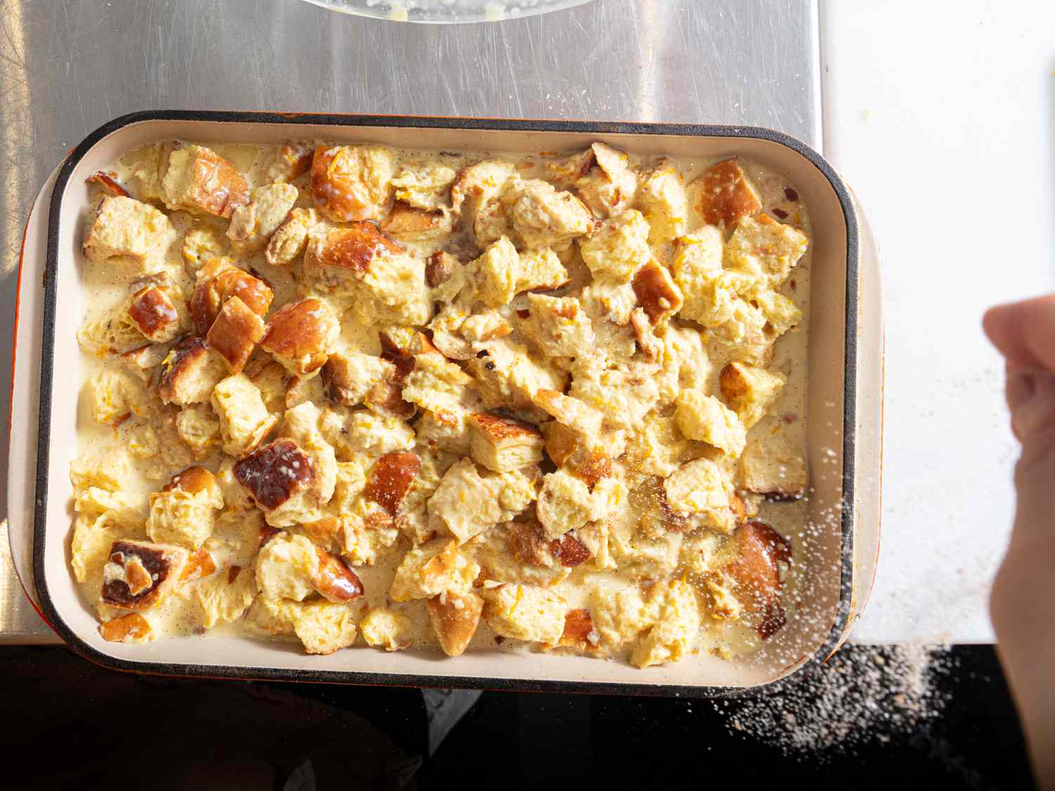 sprinkling bread pudding in baking sheet with cugar and cinnamon 